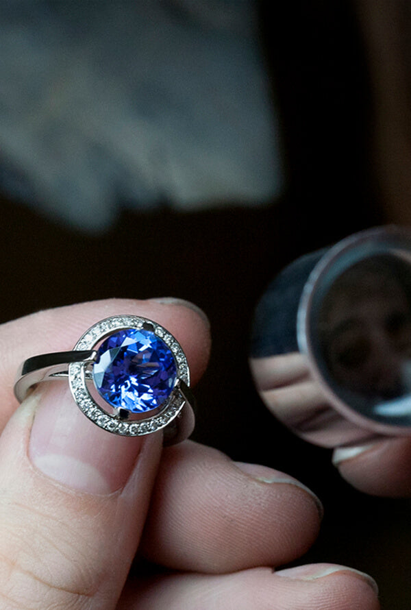 A platinum ring set with a large Tsavorite and diamonds being held by a jeweller as they examine the stone through a jewelers loop.